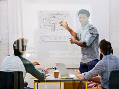 In a meeting, a man is showing his design on a board to other participants