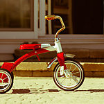 Child's rusted red tricycle standing ready. 