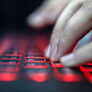 Close up of the hands of a woman typing on a red lit laptop keyboard. 