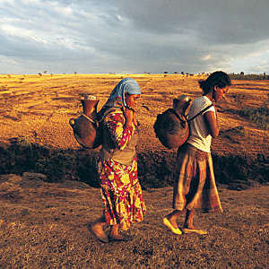 Two African women carrying terracotta water pots on their backs.