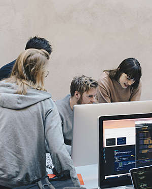 Group of four young people working together on a computer in an office environment.