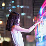 Young woman using a large interactive screen on a Shanghai street at night.