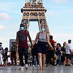 Couple wearing a protective mask walk a front the Eiffel Tower in France.